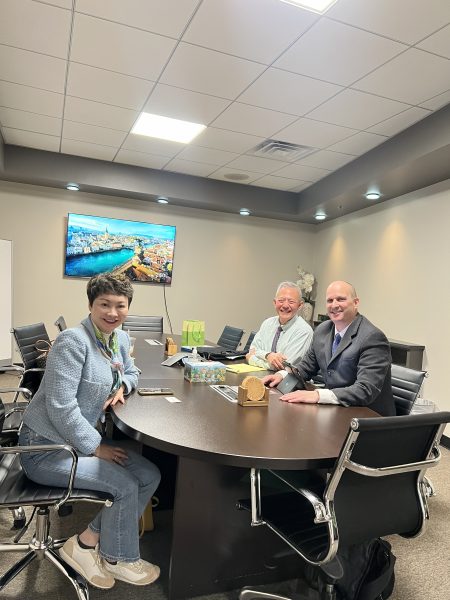 RCIC Cellia Xiao sitting at a conference table with two lawyers specializing in criminal defense. The meeting is taking place in a well-lit room, with a screen displaying a scenic view in the background