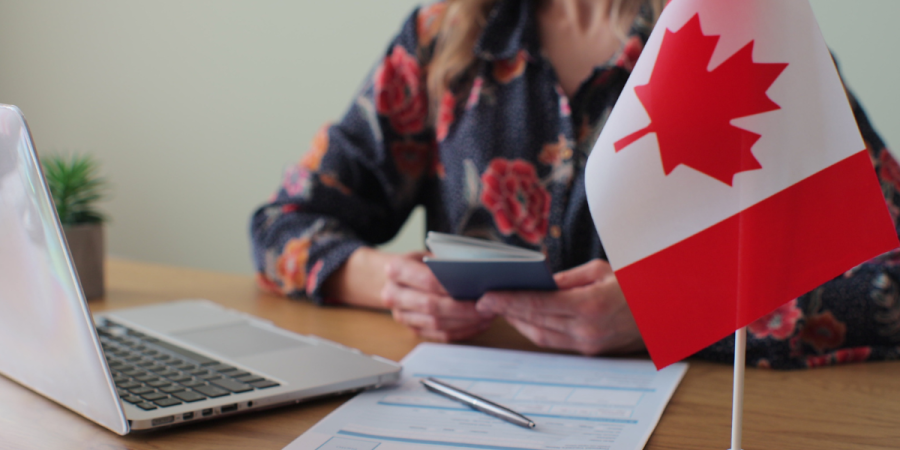 Immigration Consultant vs DIY Startup Visa: A person holding a passport at a desk with a laptop, visa application form, and a Canadian flag, symbolizing the decision-making process for a Canada Startup Visa application.