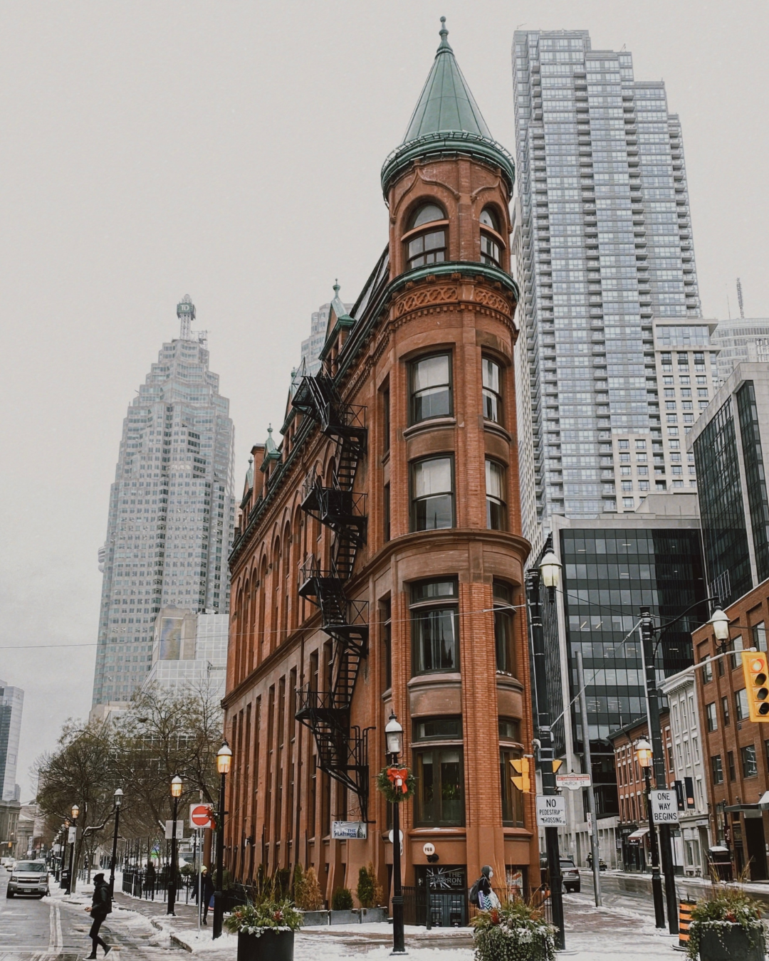 Historic Gooderham Flatiron Building in Toronto on a snowy day, surrounded by modern skyscrapers and light pedestrian traffic.

