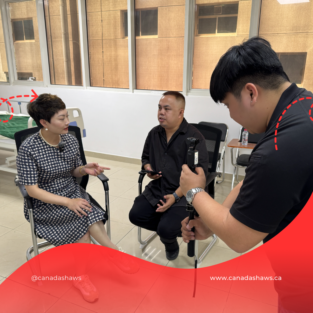 “Behind-the-scenes photo of a video interview at a training facility. Cellia Xiao is being interviewed by a media representative while a cameraman films the session. Hospital beds and large windows are visible in the background.”