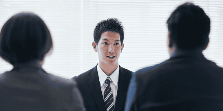 immigration interview with a man in a suit talking to two interviewers.